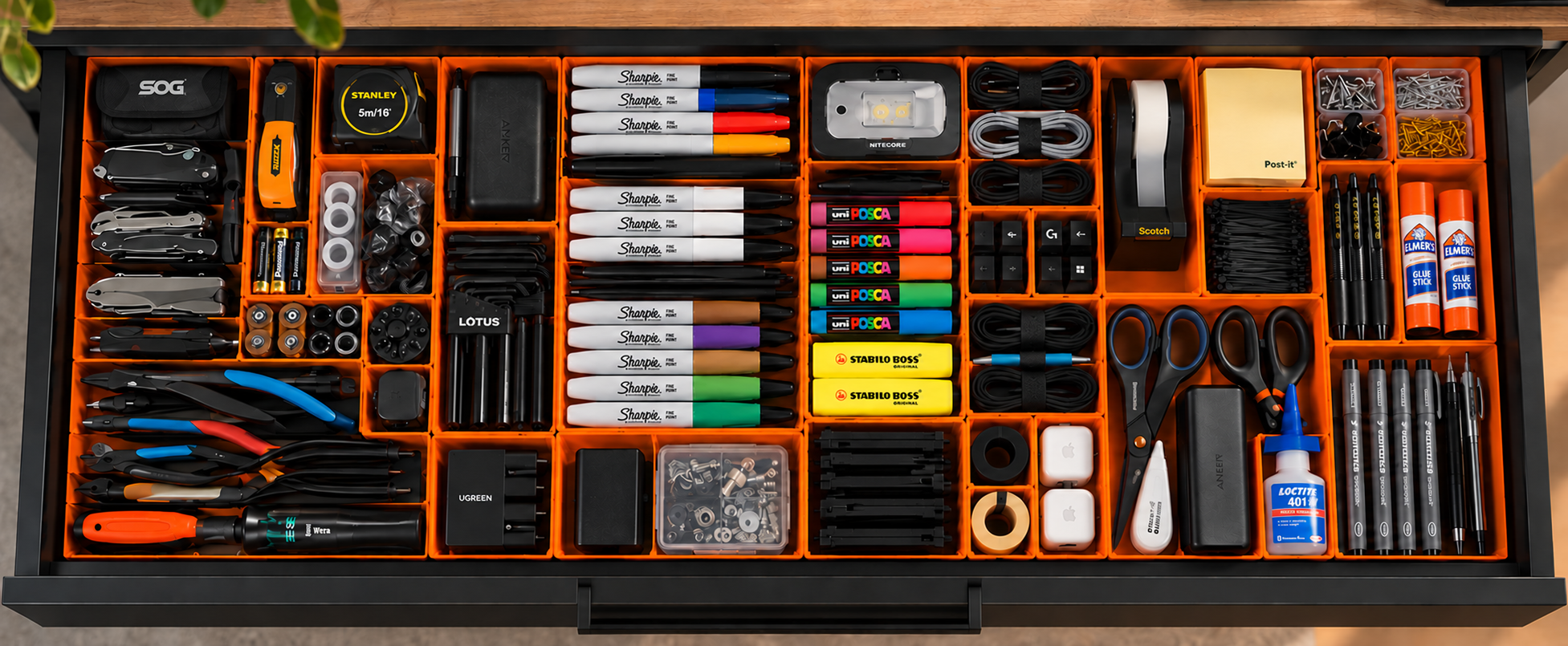 An open drawer organized with orange Gridfinity bins, tools, cables, and stationery